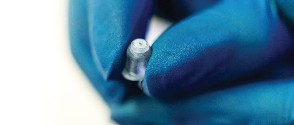 A microneedle is held by a hand in a blue glove